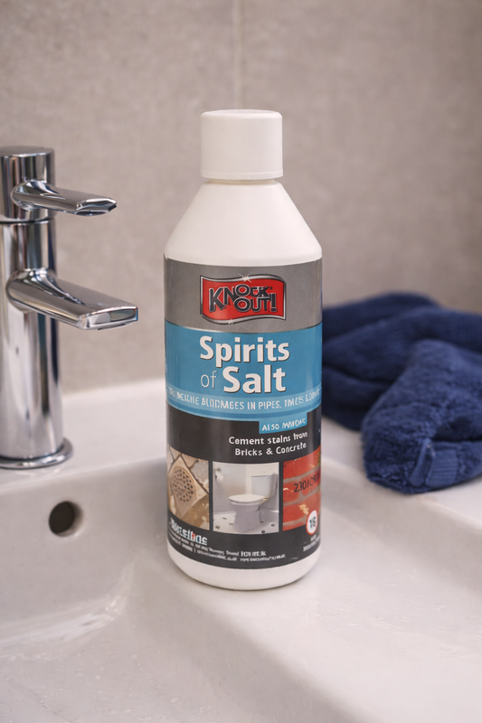Bottle of 'Knock-N-Out Spirits of Salt' on a bathroom counter with a faucet and towel in the background.